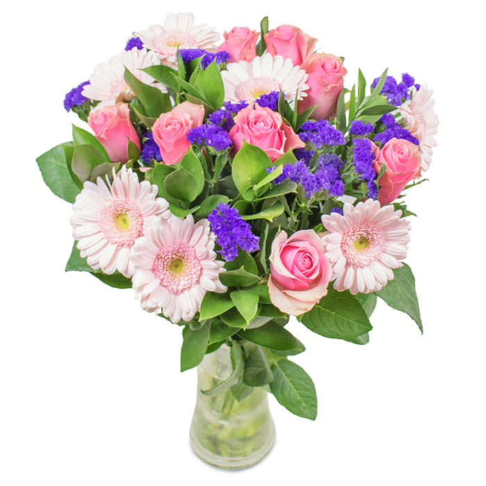 A stunning, artisan-arranged bouquet from a Brockley florist, set within a sleek clear glass vase and photographed against a clean white background. Soft- to medium-pink roses, numbering around eight and varying from tight spirals to half-open blooms, form the heart of the arrangement. Interwoven are about half a dozen pale pink gerbera daisies, their large round blooms and cream-tinted centers adding fullness and serenity. Bold highlights arrive via small clusters of deep purple statice, offering visual and textural contrast while echoing the artistic spirit of Brockley's nearby art galleries and studios. Lush, deeply green leaves encircle and support the flowers, giving a sense of abundance akin to the thriving local gardens. The visible stems and water in the vase enhance the impression of day-fresh picking, as if just delivered from a Brockley florist. This bouquet is a perfect gift for birthdays, anniversaries, or Mother's Day, offering joy and affection in every carefully crafted detail-a true piece of Brockley's floral artistry brought indoors.
